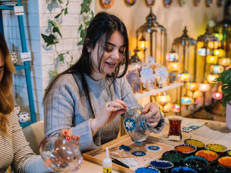 Woman making a mosaic lamp surrounded by glowing lamps